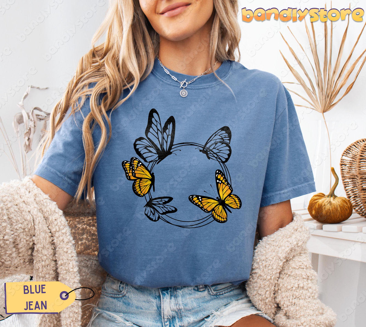 Monarch Butterfly Wreath T-Shirt in Blue Jean on a model facing forward amid dried plants and a pumpkin.