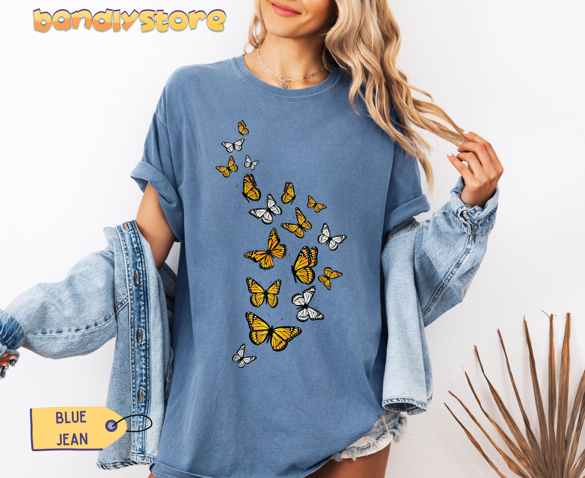 Monarch Butterfly Flock T-Shirt in Blue Jean, worn front-facing with denim jacket and dried palm nearby.