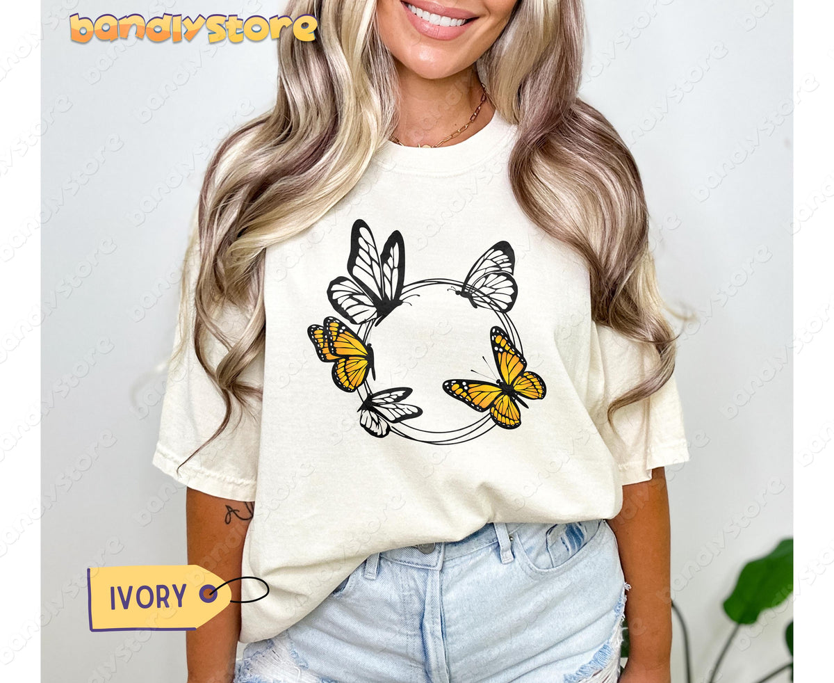 Monarch Butterfly Wreath T-Shirt in ivory, worn by a smiling woman facing forward with blonde hair and jeans.