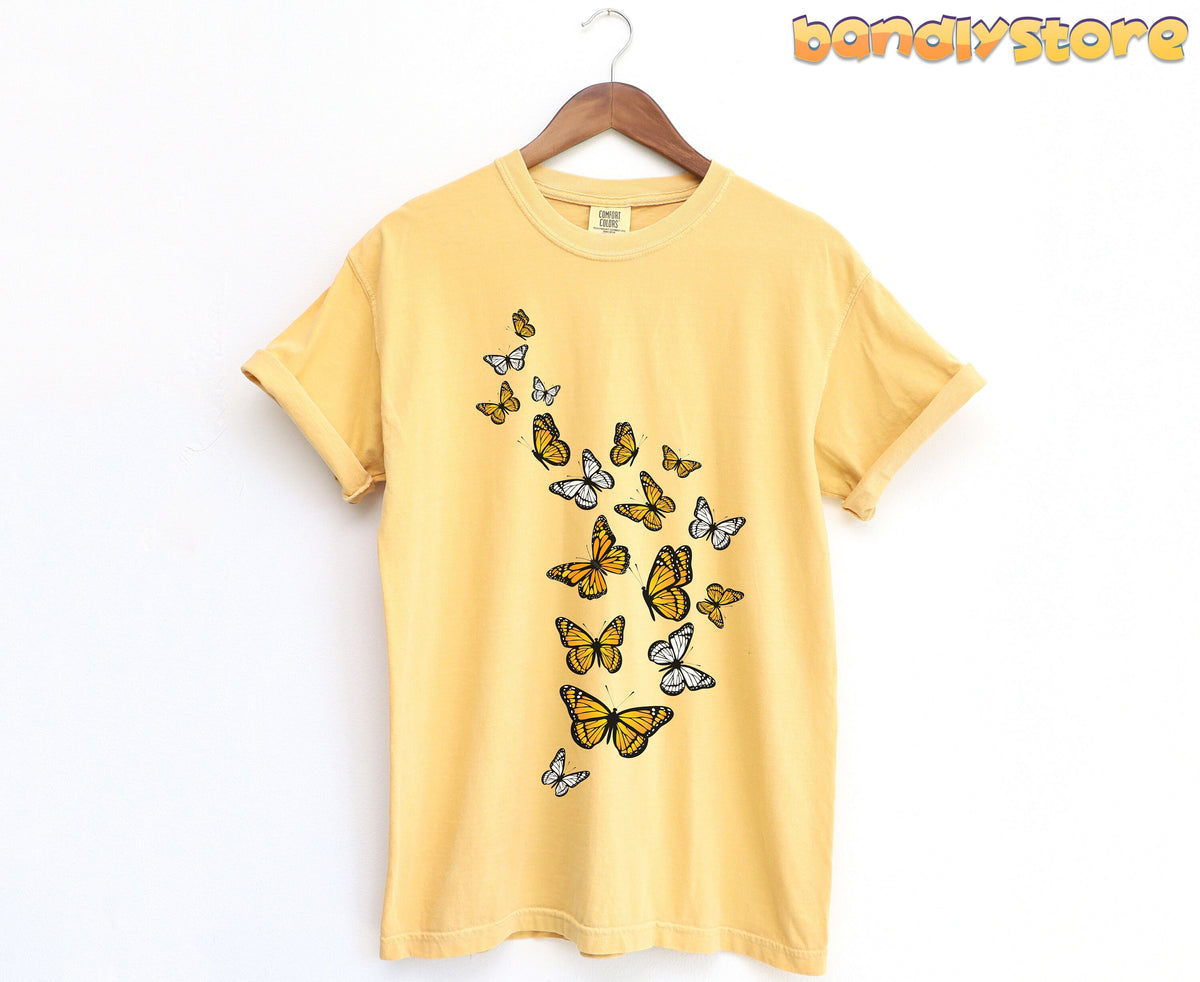 Monarch Butterfly Flock T-Shirt in mustard hanging on a wooden hanger against a plain white wall.