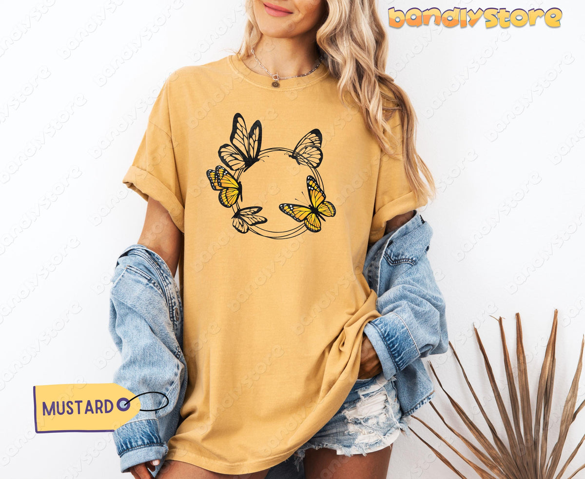 Monarch Butterfly Wreath T-Shirt in mustard on a model against a white wall with denim jacket and dried palm leaves.