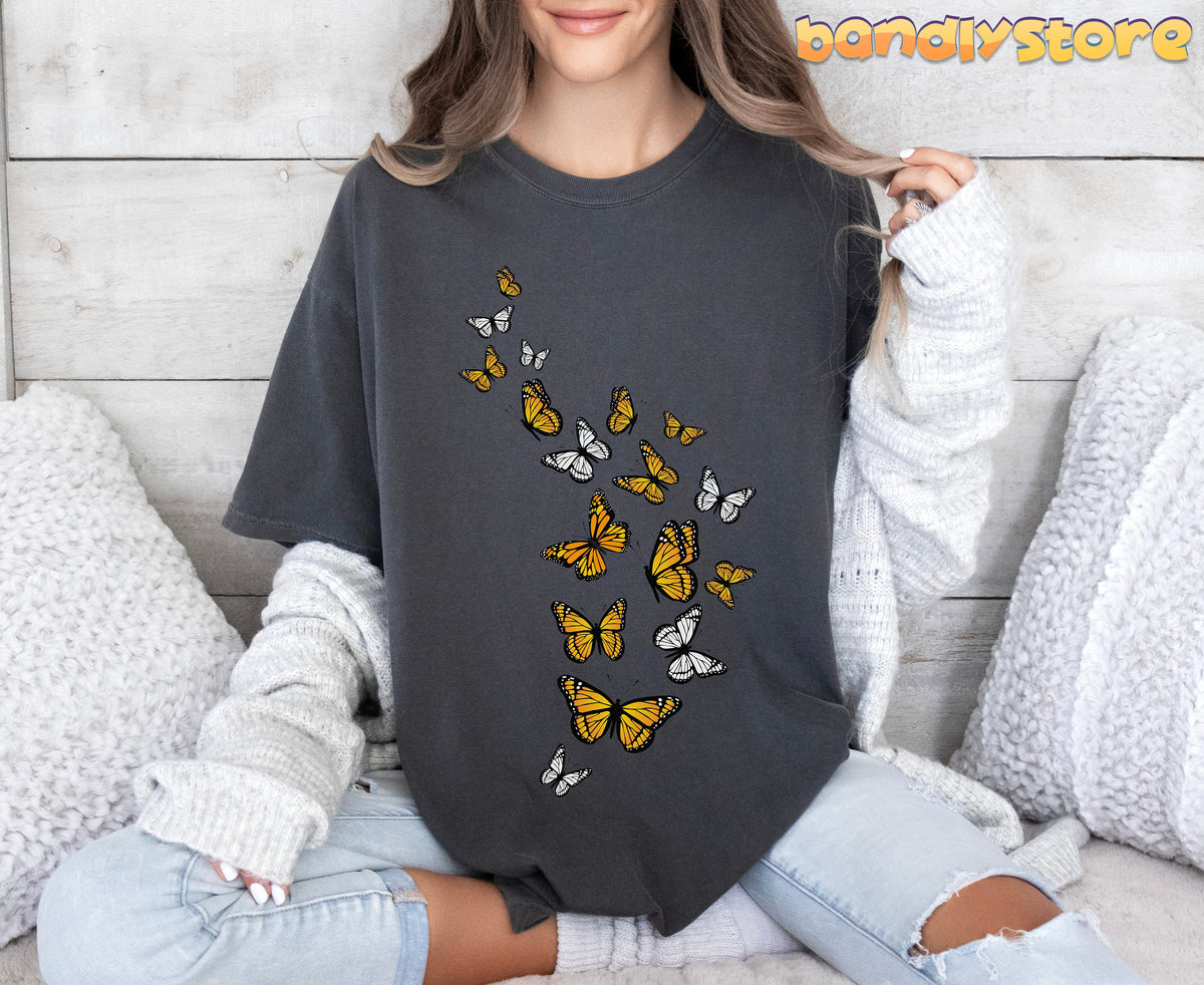 Monarch Butterfly Flock T-Shirt in pepper on a seated person against wooden wall with white pillows.