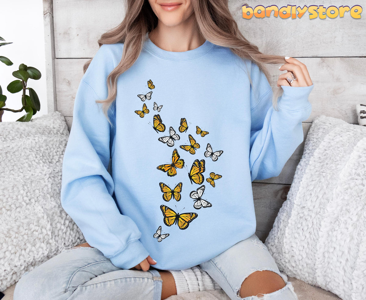 Monarch Butterfly Flock Sweatshirt in light blue on a seated person among pillows against a wooden wall.