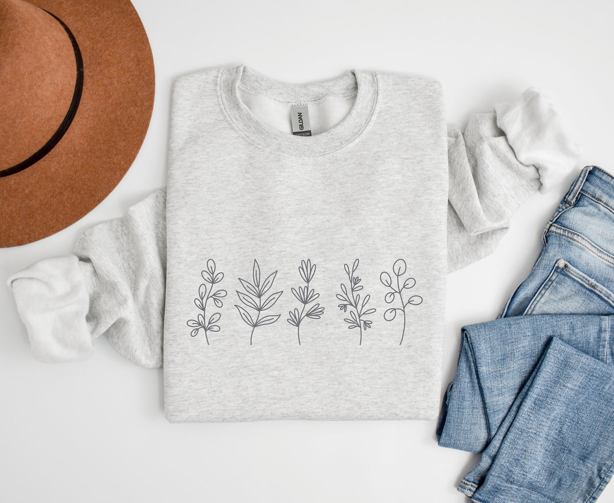 Monochrome Floral Sweatshirt in ash folded flat from above beside a brown hat and blue jeans.