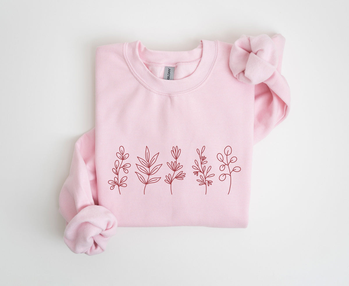 Monochrome Floral Sweatshirt in light pink, folded flat on white with sleeves knotted and five reddish plant line drawings across the chest.