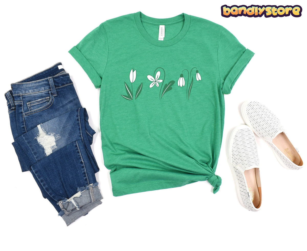 Monochromatic Spring Flowers T-Shirt in Heather Kelly laid flat beside ripped jeans and white slip-on shoes.