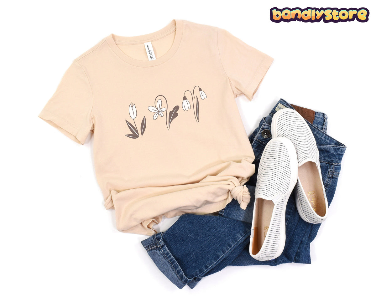 Monochromatic Spring Flowers T-Shirt in Soft Cream laid flat beside jeans and slip-ons on a white background.