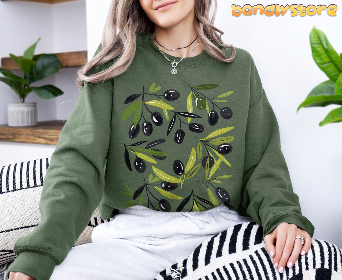 Olives Sweatshirt in military green on a seated person amid houseplants and geometric cushions.
