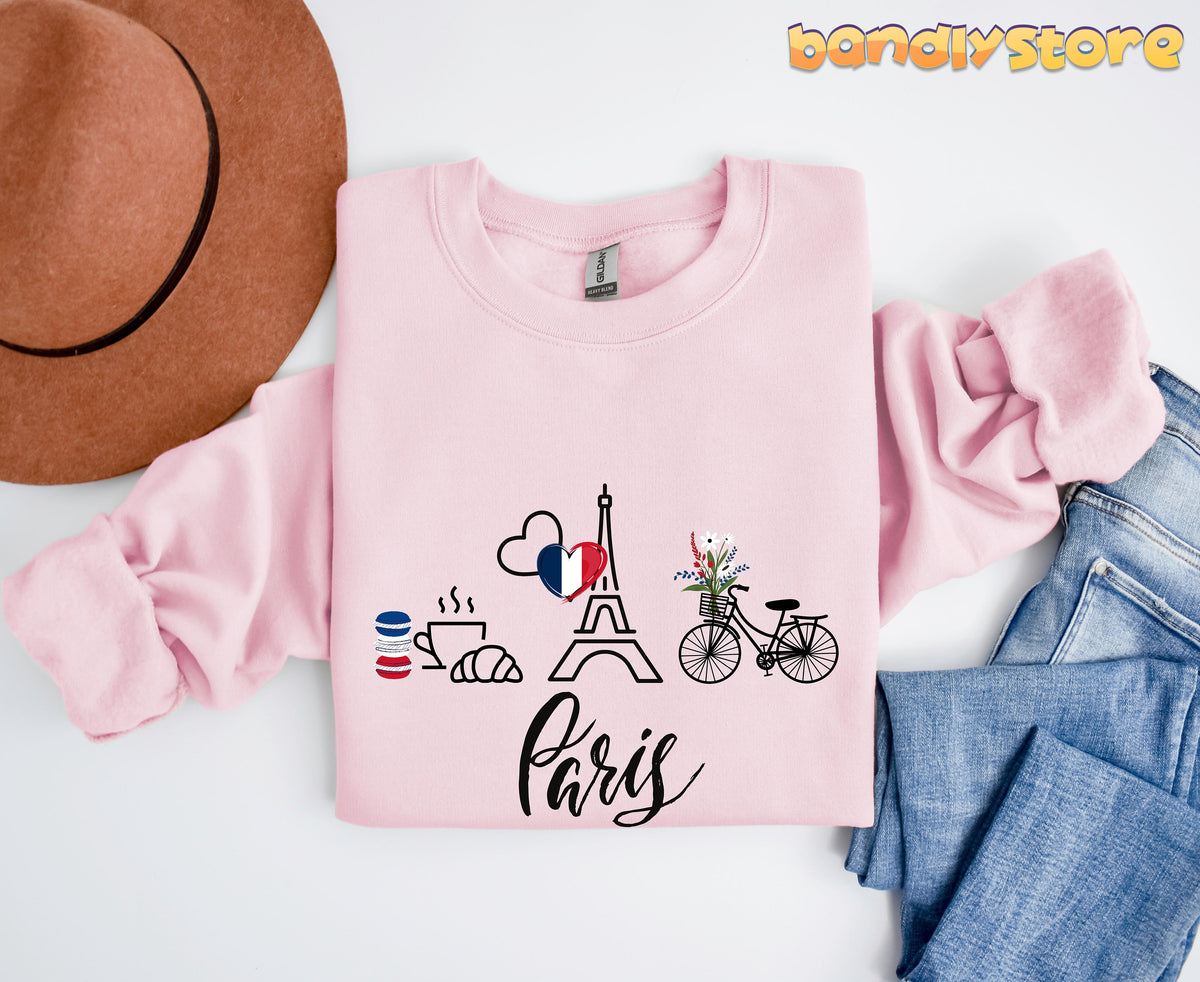 Paris Eiffel Tower Sweatshirt in light pink laid flat beside a brown hat and blue jeans.