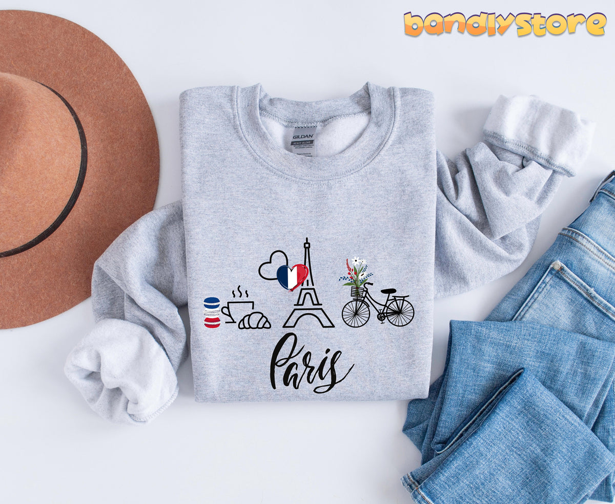Paris Eiffel Tower Sweatshirt in Sport Grey flat-laid next to a brown hat and blue jeans.