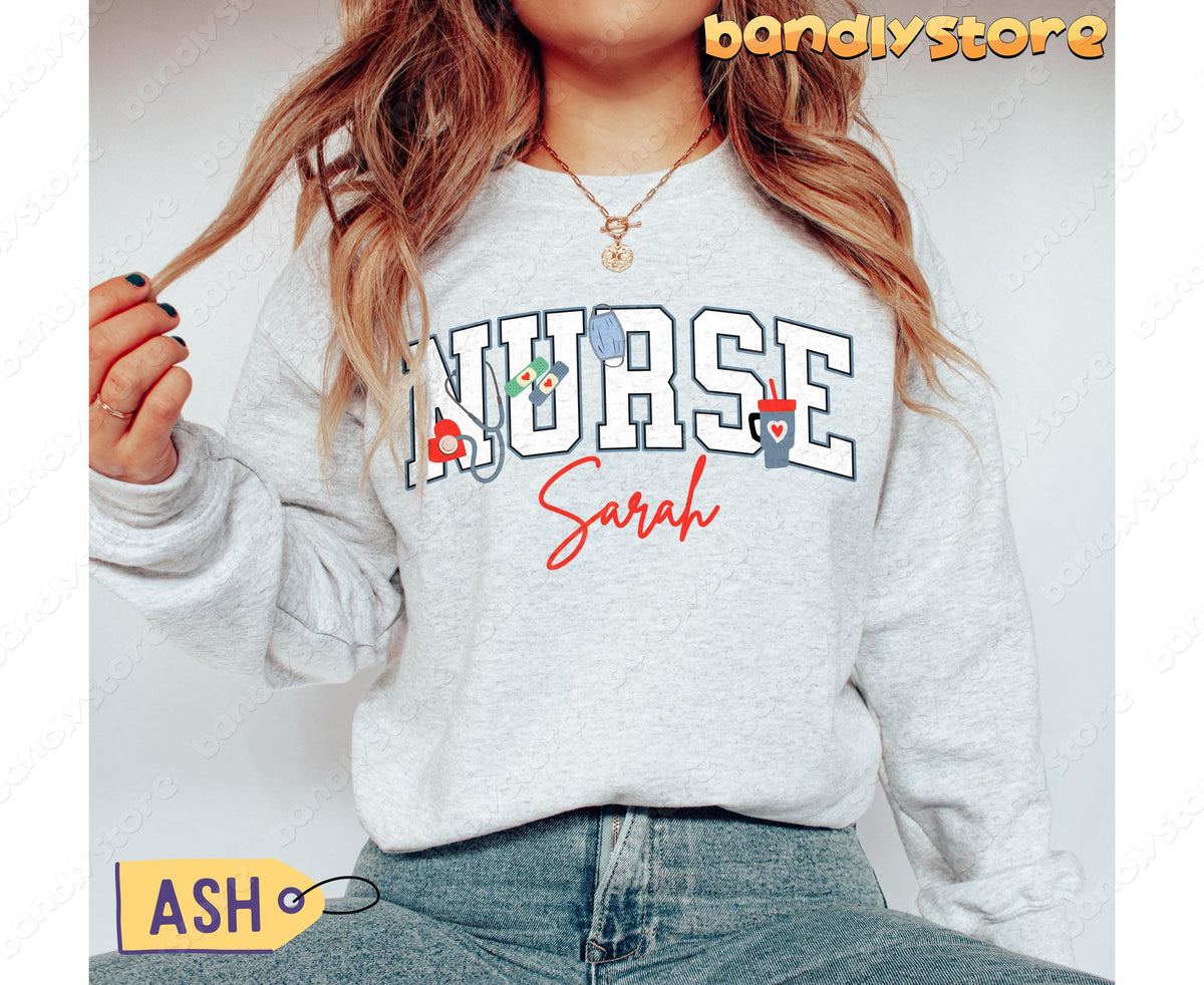 Personalized Nurse Sweatshirt in ash on a person with long wavy hair, front view, jeans and ASH tag visible.