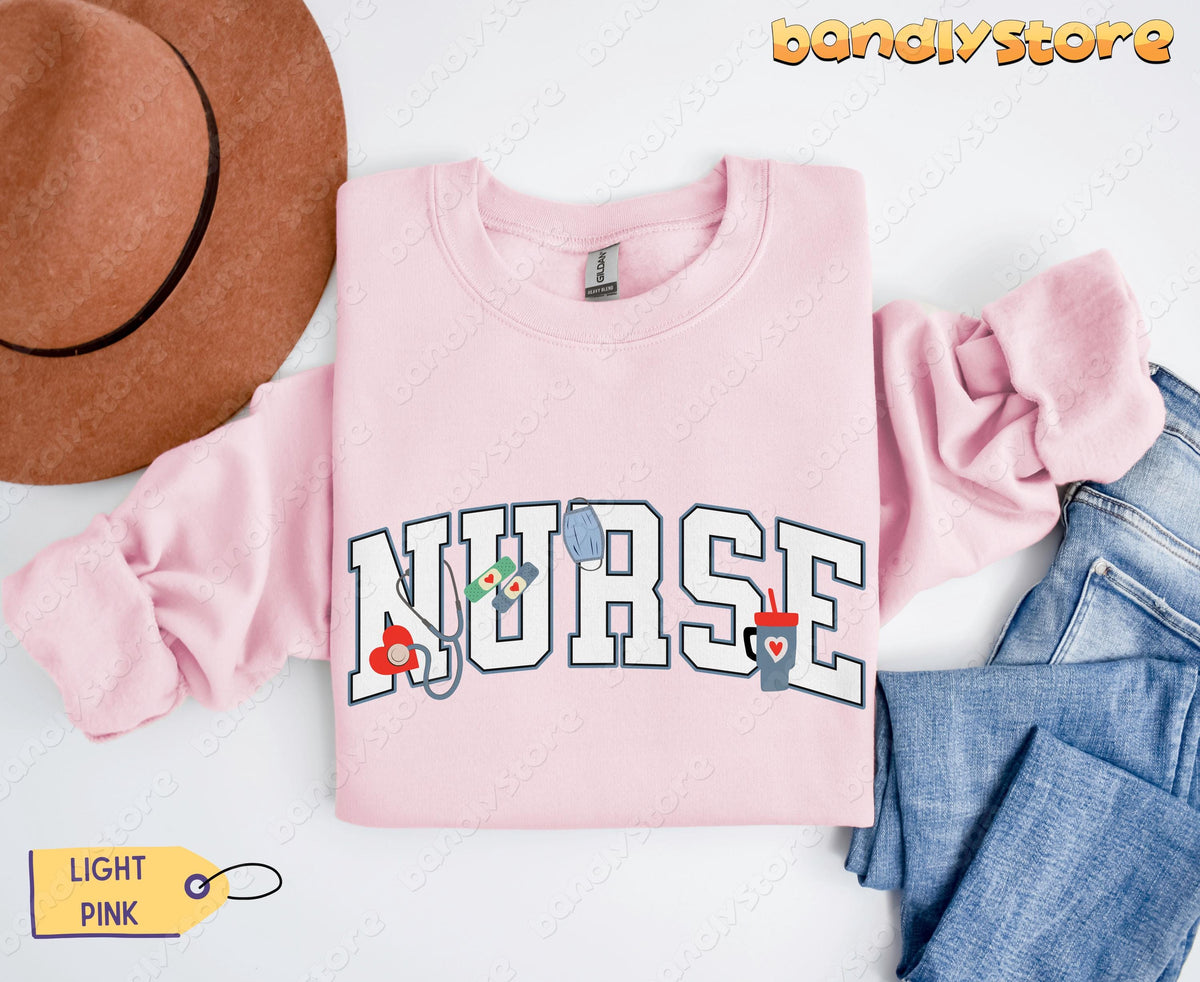 Personalized Nurse Sweatshirt in light pink, folded flat beside a brown hat and blue jeans.