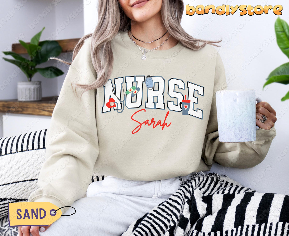 Personalized Nurse Sweatshirt in sand on seated woman holding mug beside plants and striped blanket.