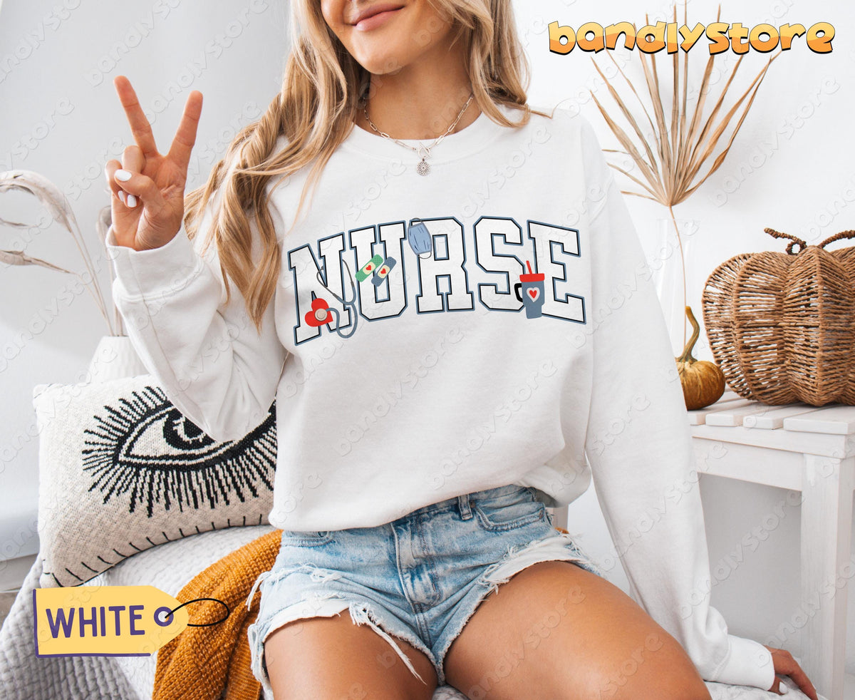 Personalized Nurse Sweatshirt in white on a woman giving a peace sign amid pillows, dried plants and baskets.
