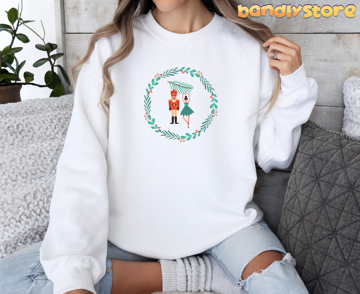 Nutcracker Ballet Sweatshirt in white, worn by a seated model amid sofa pillows and a plant.