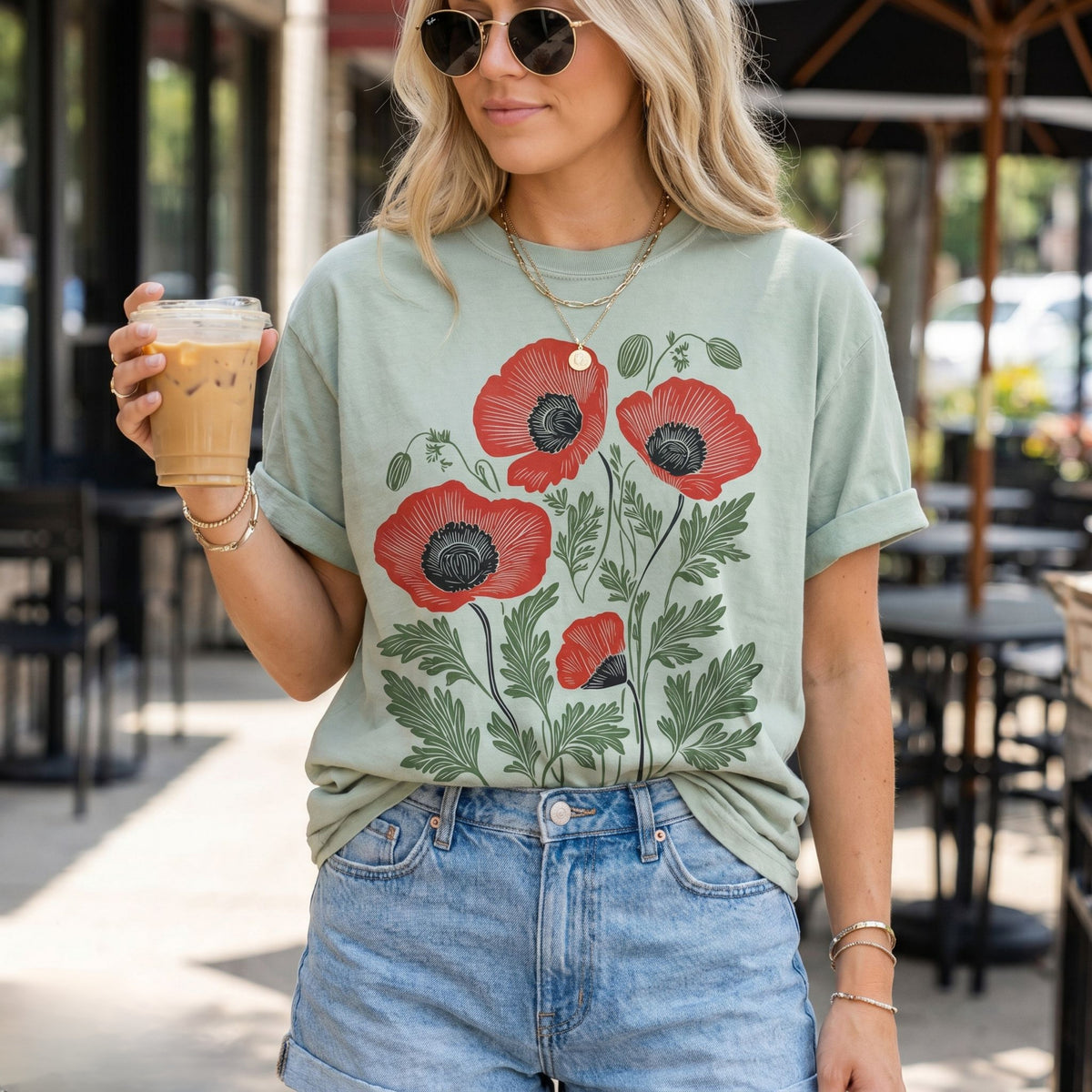 Poppies Linocut T-Shirt in bay worn by a woman holding iced coffee at an outdoor cafe patio.