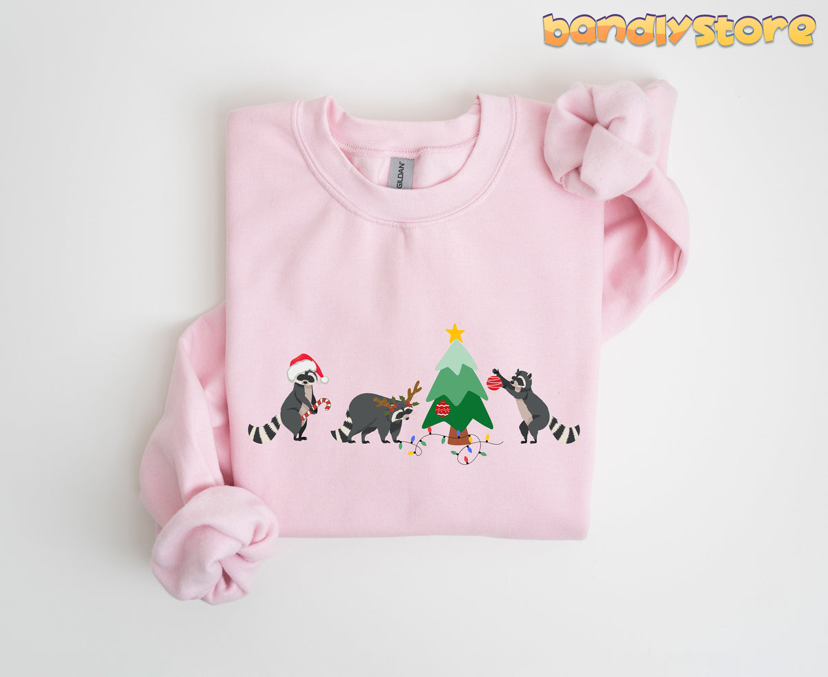 Raccoon Christmas Sweatshirt in light pink folded flat on white background showing raccoons decorating a tree.