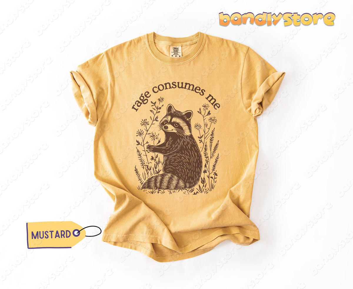 Rage Consumes Me T-Shirt in mustard laid flat on white background with raccoon among plants graphic.