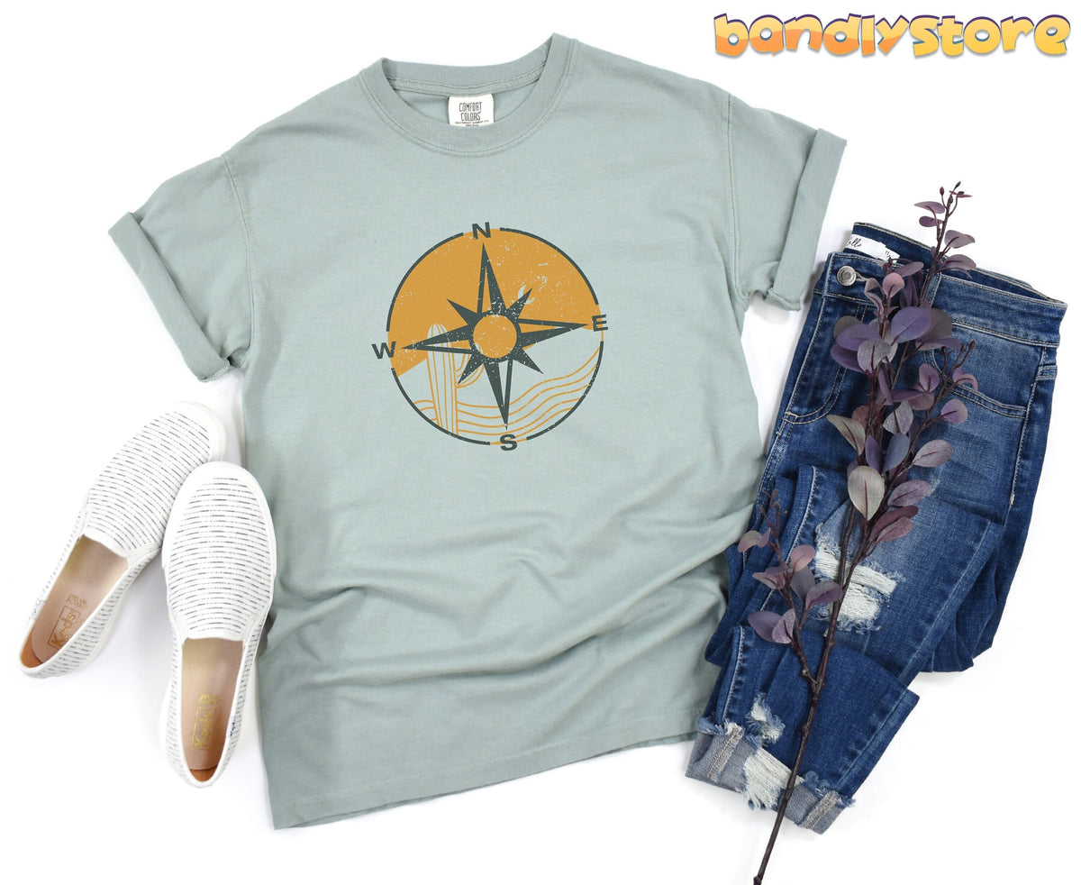 Retro Compass T-Shirt in Bay, flat lay with white slip-ons, ripped blue jeans and purple foliage.