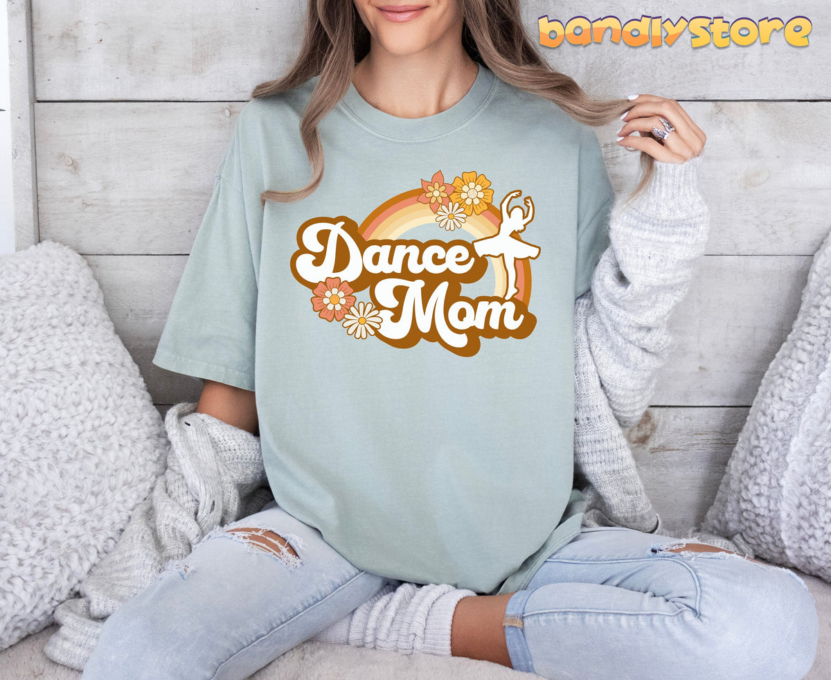 Retro Dance Mom T-Shirt in Bay, worn by a seated person against a light wood wall with white pillows nearby.