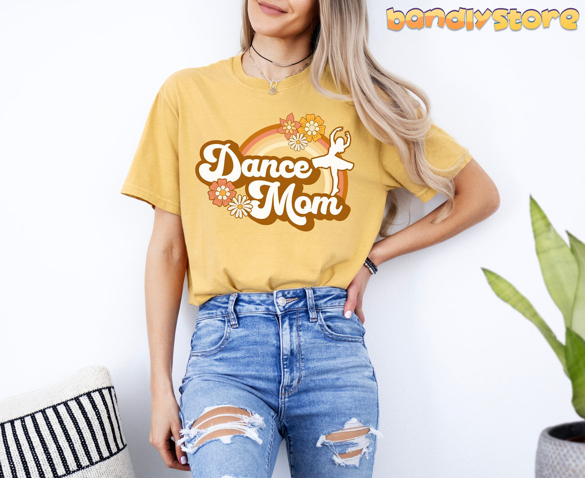 Retro Dance Mom T-Shirt in mustard on a woman facing forward against a white wall near a striped pillow and plant.