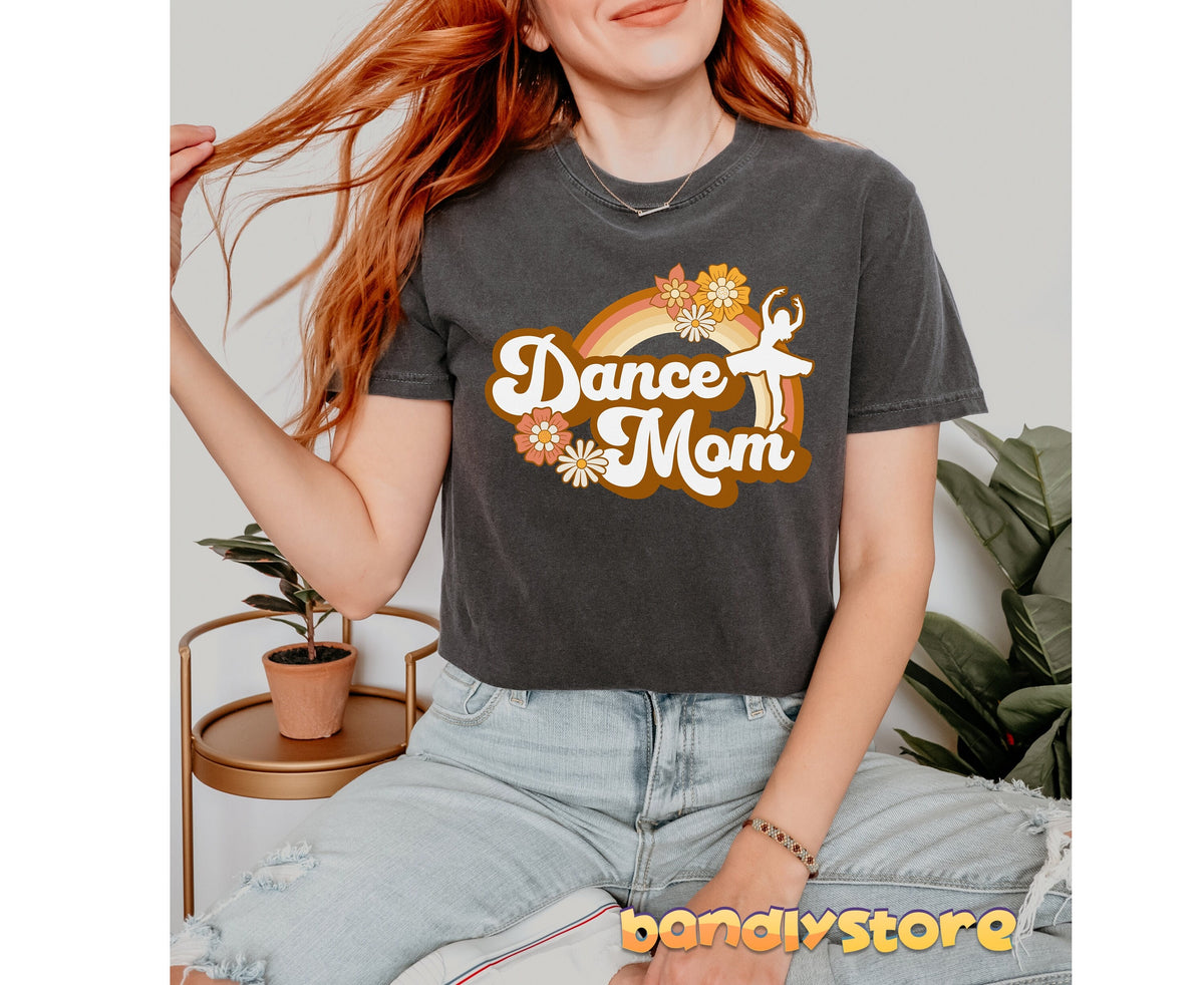 Retro Dance Mom T-Shirt in pepper on a seated red-haired woman indoors beside plants and a gold side table.