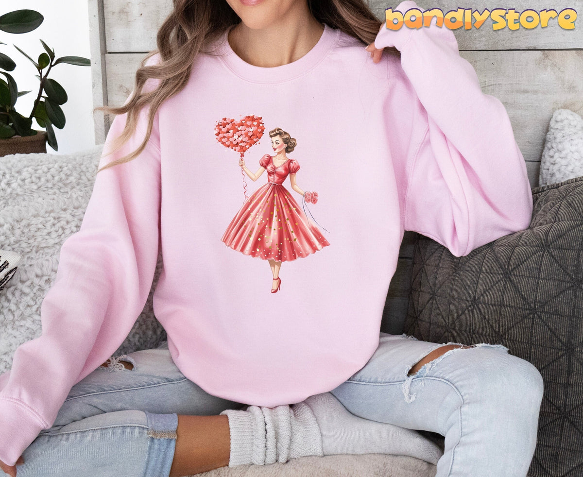 Cute Valentine Girl Sweatshirt on light pink fabric, modeled seated indoors amid pillows and a plant.