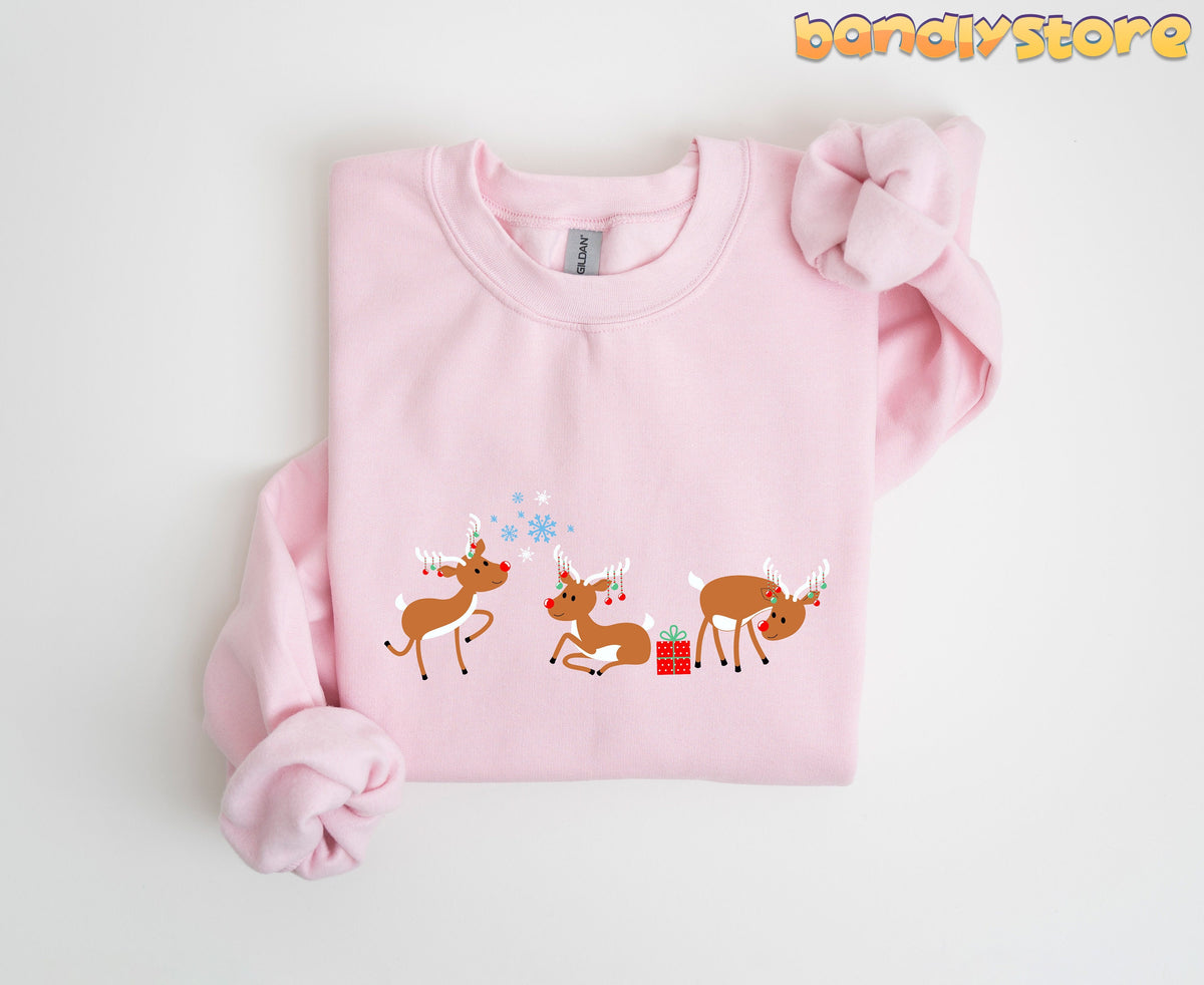 Rudolph The Red Nosed Reindeer Sweatshirt in light pink folded flat on a white background with three cartoon reindeer.
