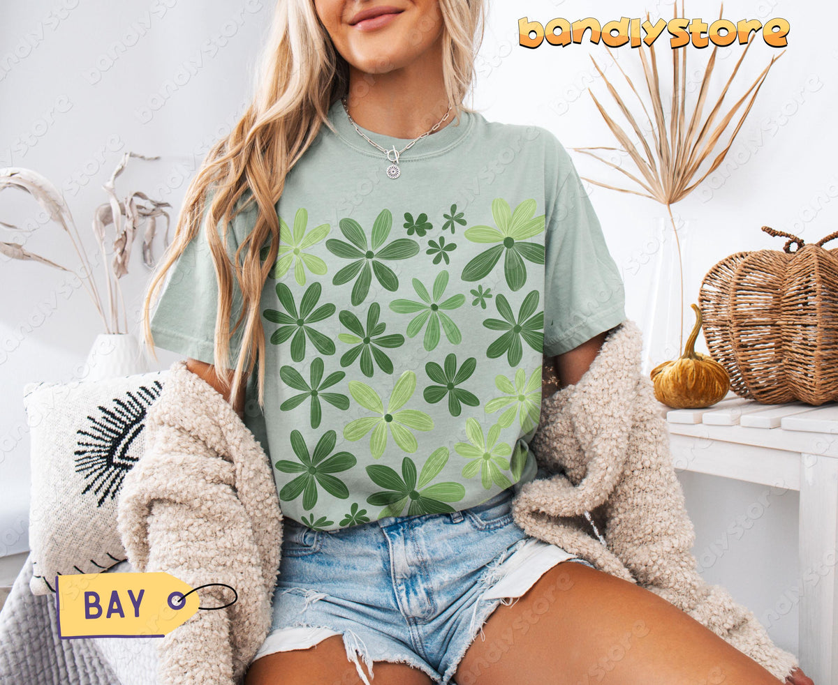 Sage Green Wildflowers T-Shirt in Bay on a seated model amid dried plants, pillows and pumpkins.