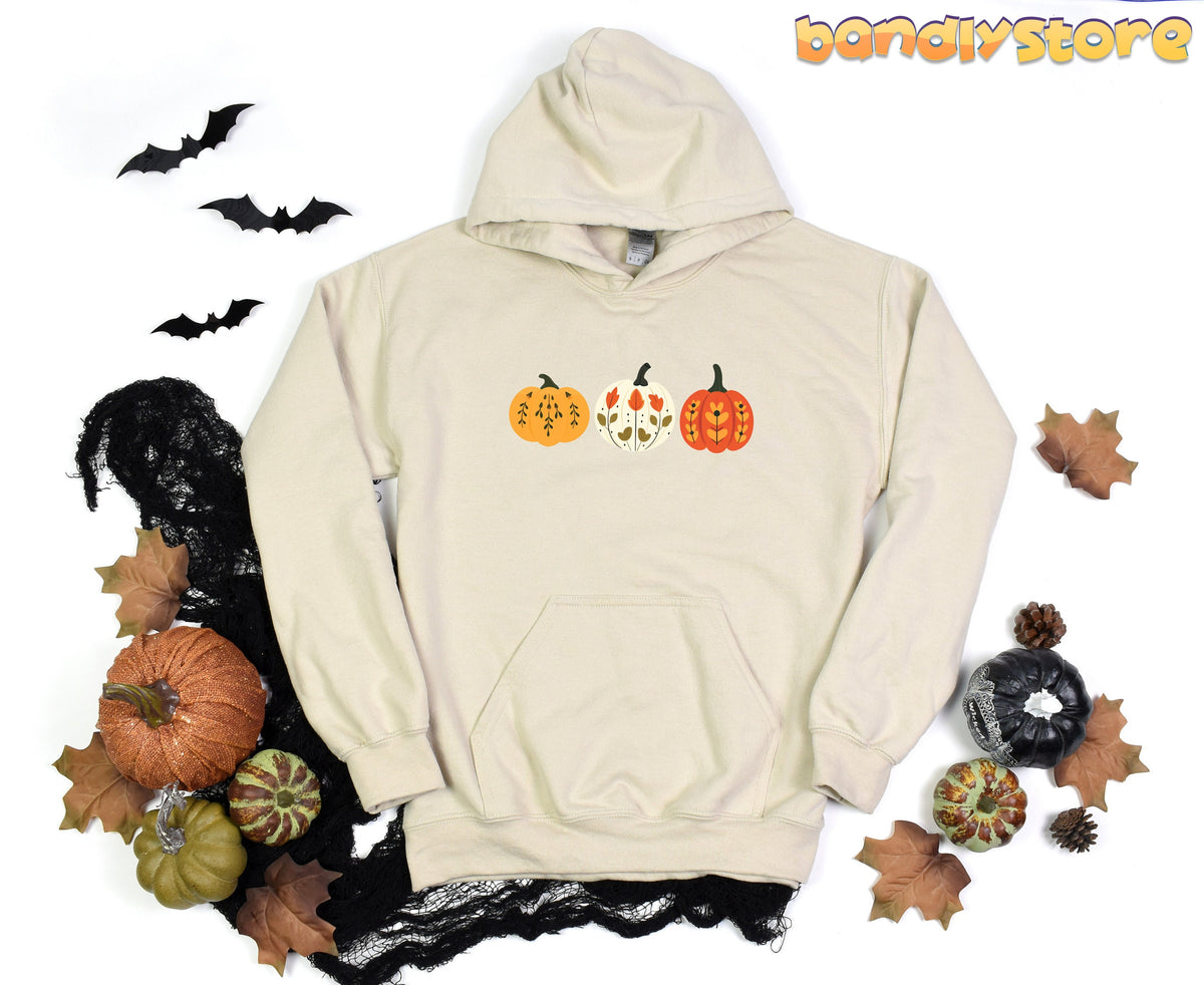 Scandinavian Art Pumpkin Hoodie in sand, flat-laid with bats, leaves, pumpkins and black webbing around it.
