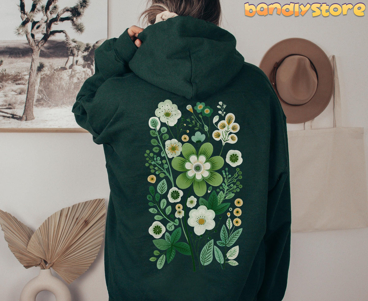 Scandinavian Wildflowers Hoodie in forest green, rear view on a person beside framed photo, hat and tote bag.