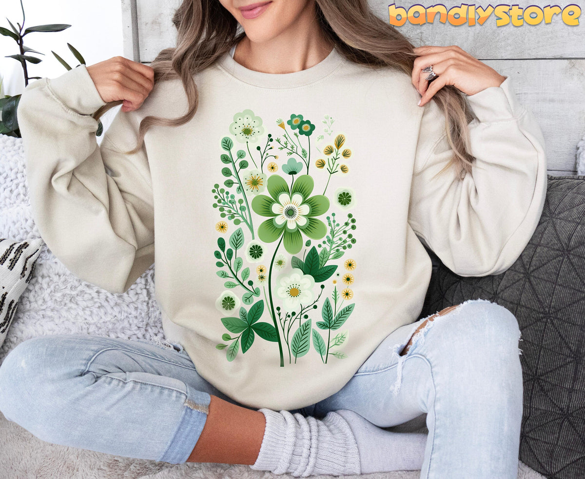 Scandinavian Wildflowers Sweatshirt in Sand on a woman sitting cross-legged amid plants and pillows.