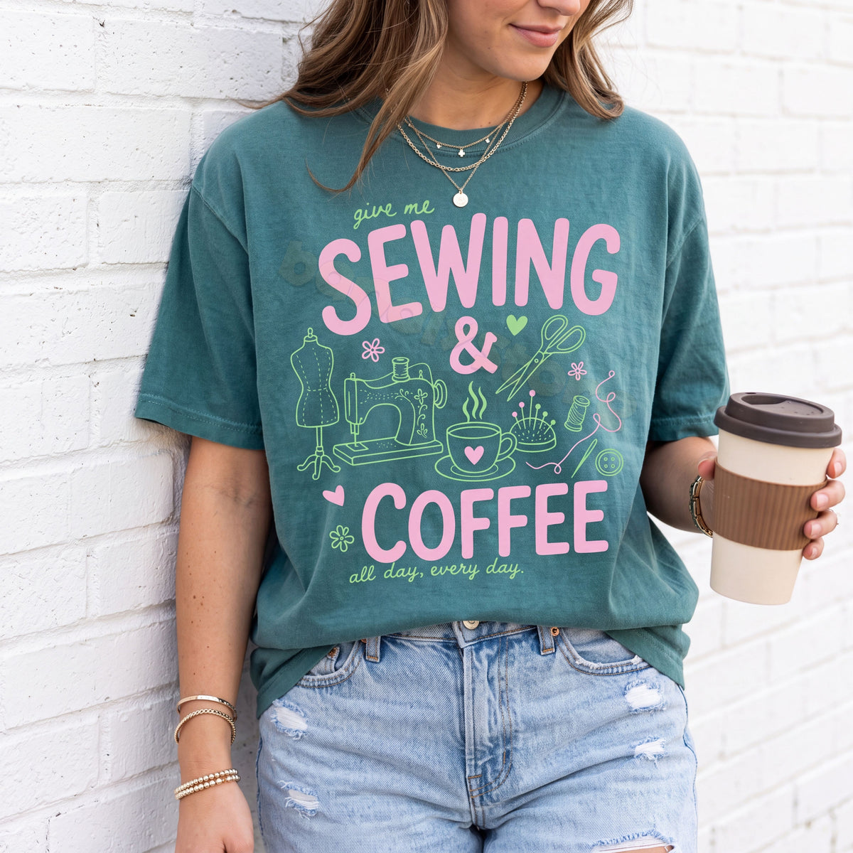 Sewing And Coffee T-Shirt in Blue Spruce, worn by a person holding a coffee cup against a white brick wall.