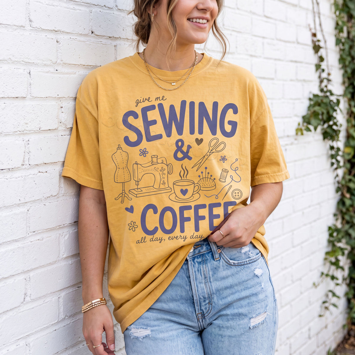 Sewing And Coffee T-Shirt in mustard on a woman leaning against a white brick wall beside greenery.