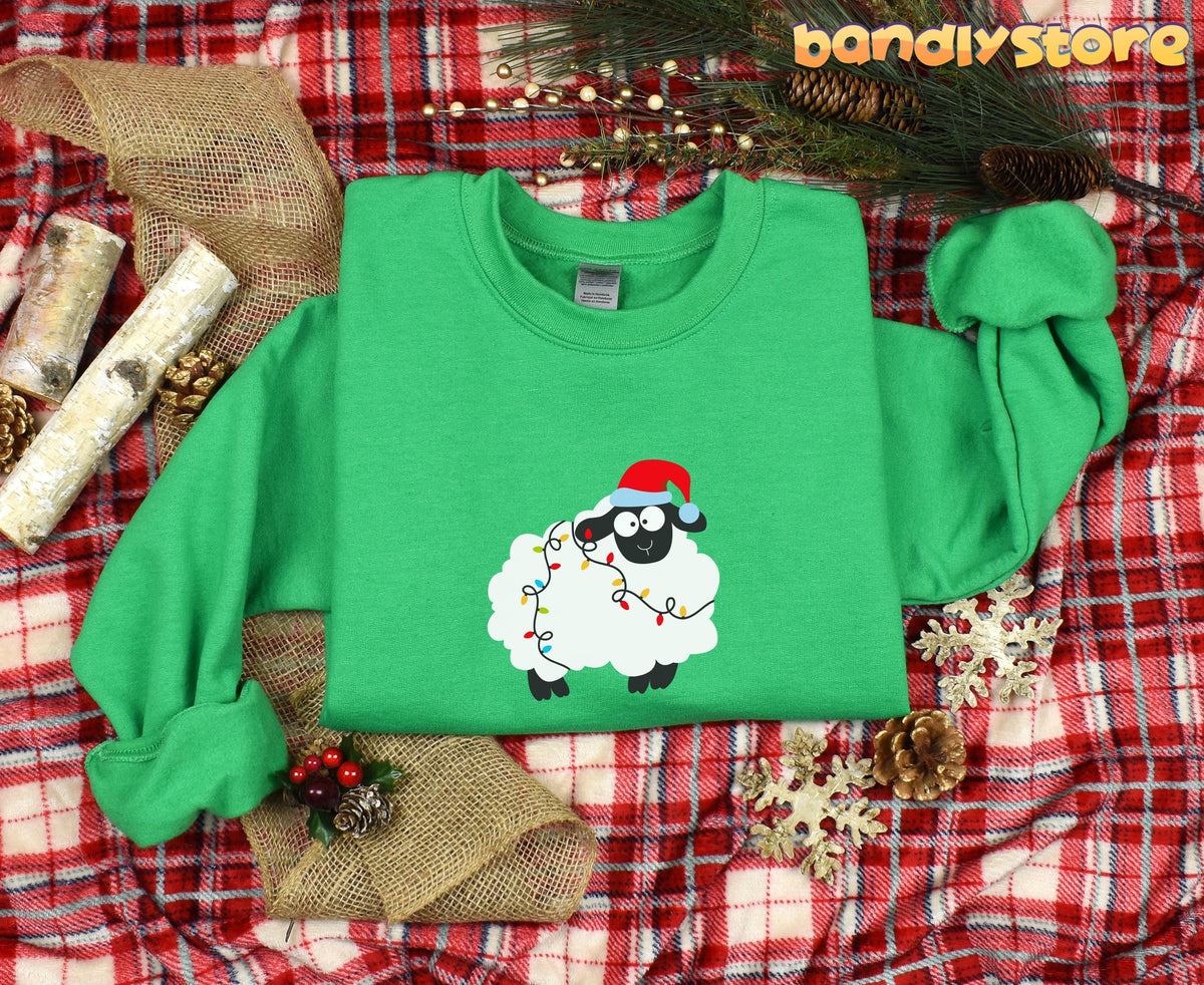 Sheep Christmas Lights Sweatshirt in Irish green, flat lay on red plaid amid pinecones, snowflakes, burlap and greenery.