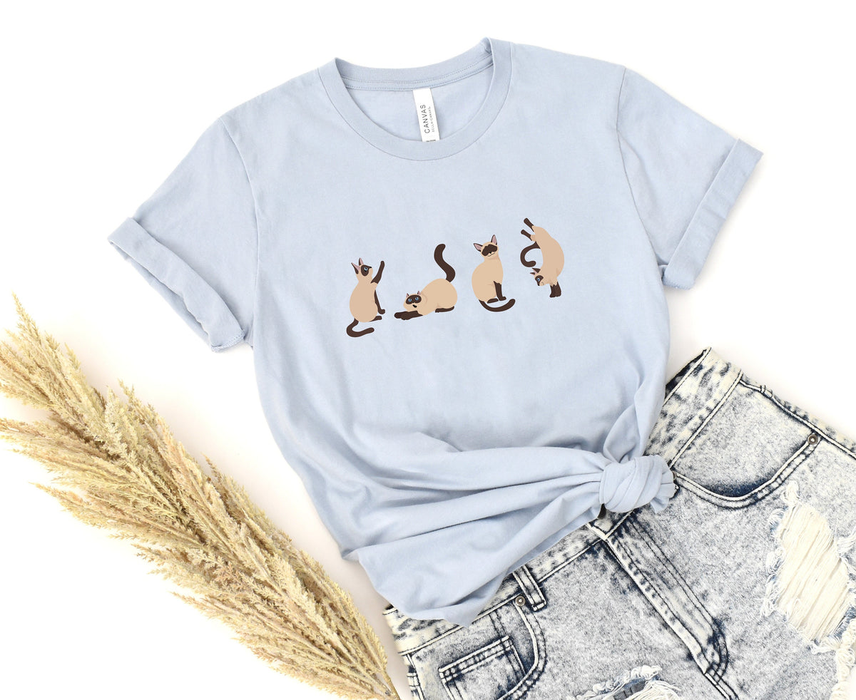 Siamese Cat T-Shirt in light blue flat-laid knotted beside ripped jeans and dried grass.
