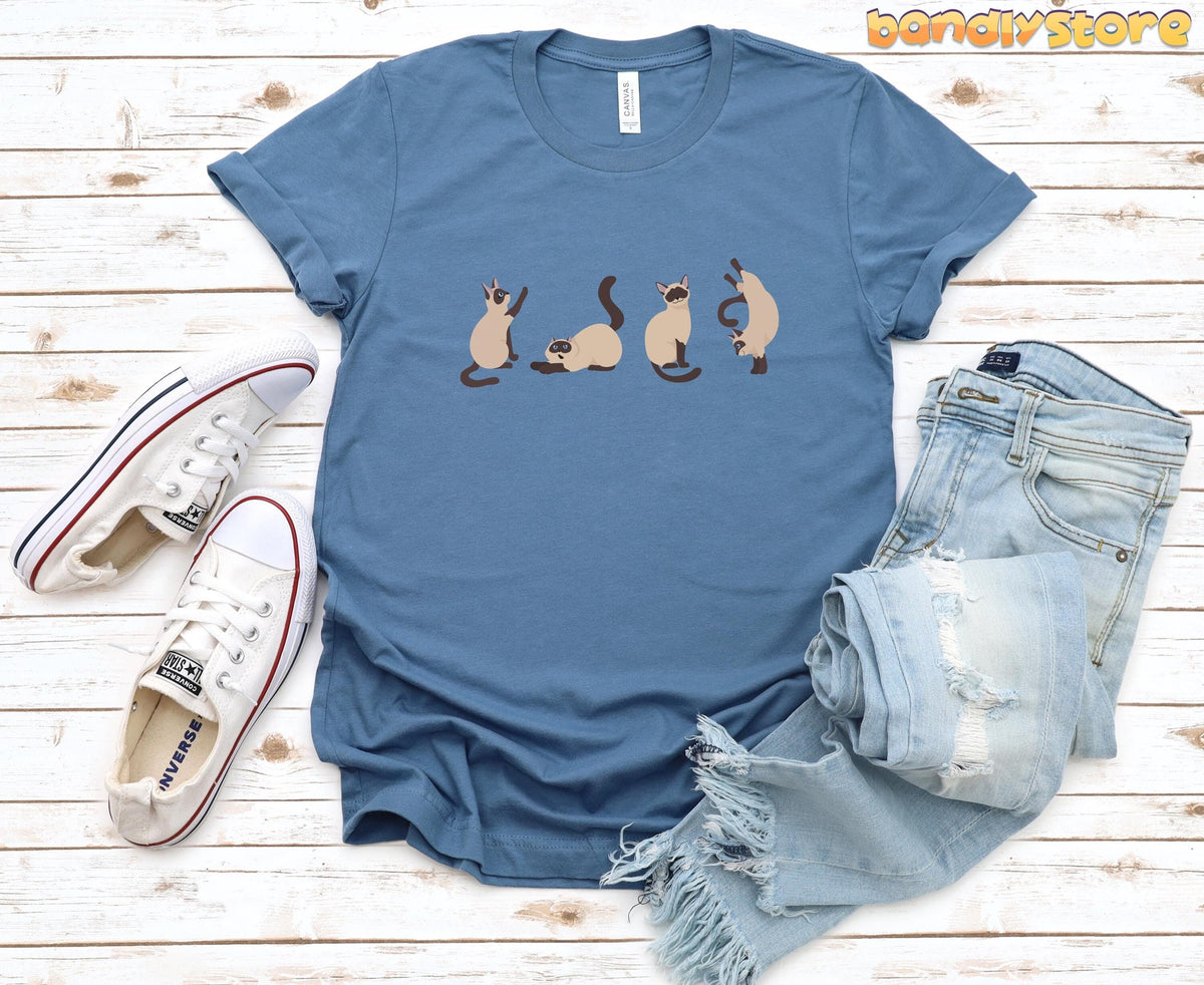 Siamese Cat T-Shirt in steel blue flat on white wood beside sneakers and ripped jeans.