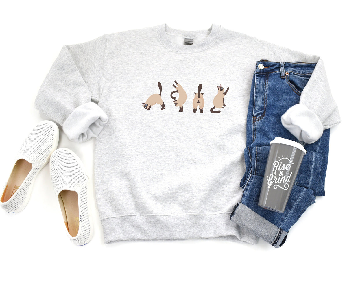 Siamese Cat Butts Sweatshirt in ash, flat-lay with white slip-ons left, jeans and Rise & Grind tumbler right.