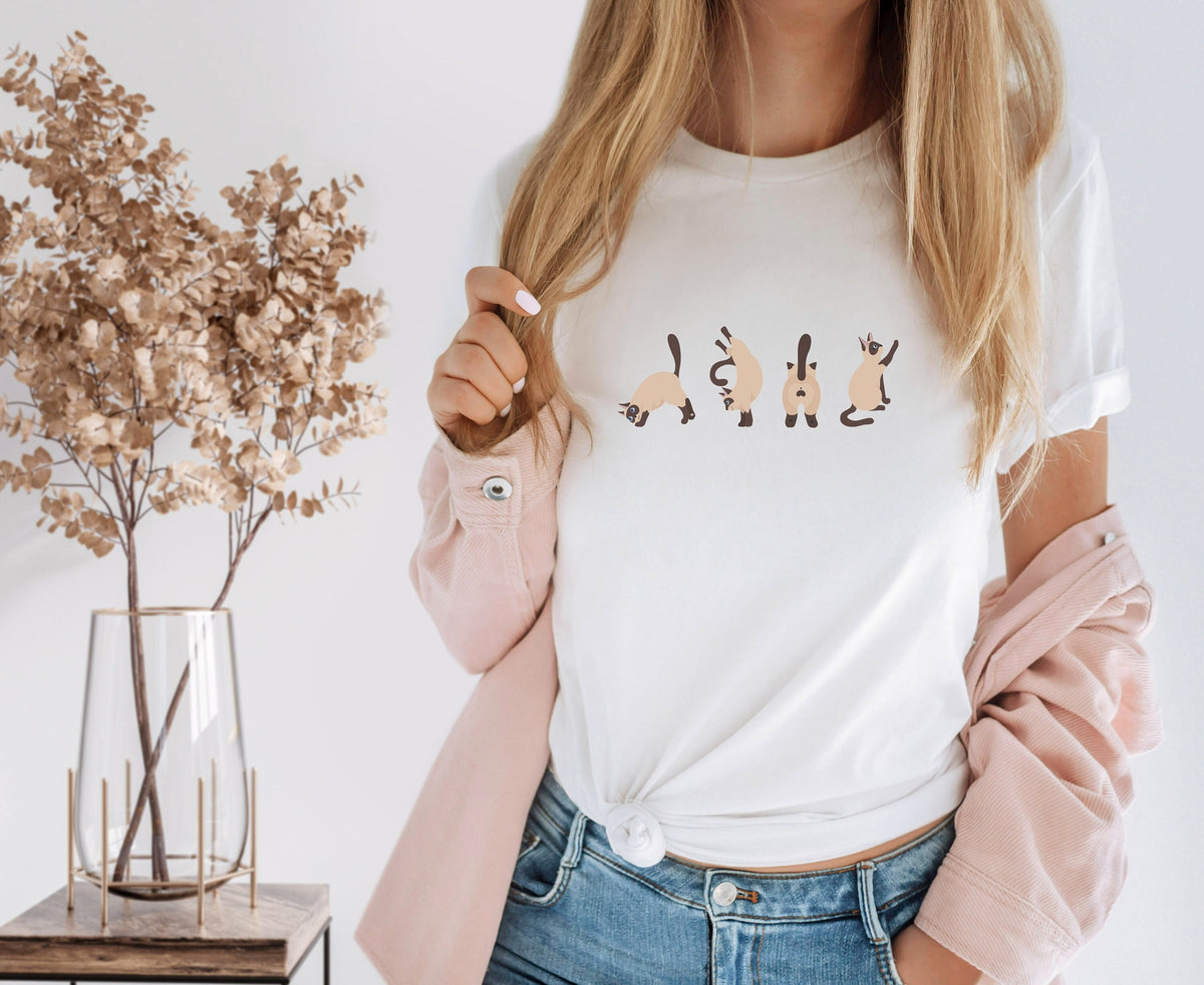 Siamese Cat T-Shirt white on a person beside a glass vase of dried plants on a wooden table.