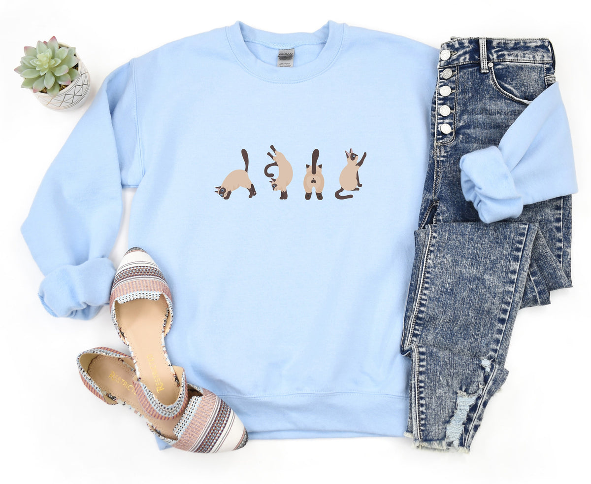 Siamese Cat Butts Sweatshirt in light blue, flat-lay with jeans, striped flats, and a small potted succulent.