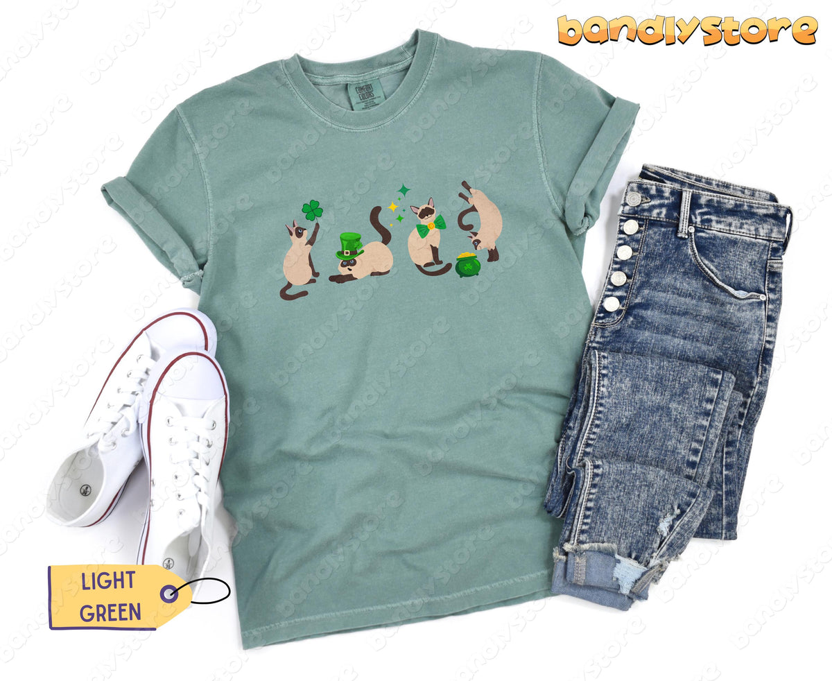 Siamese Cat Shamrock T-Shirt in light green laid flat beside white sneakers and blue jeans.