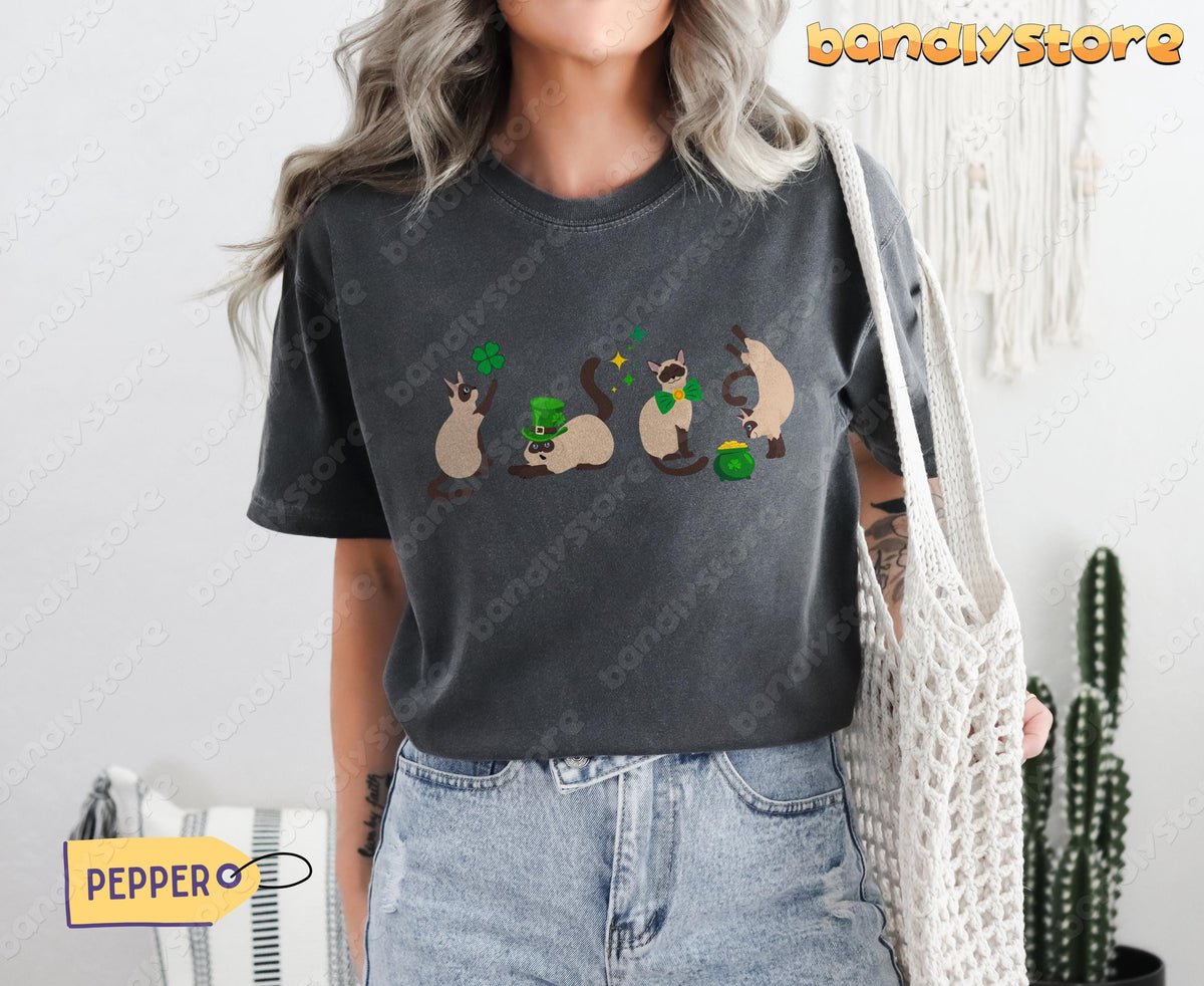 Siamese Cat Shamrock T-Shirt in Pepper on a front-facing person with white bag, jeans and houseplants.