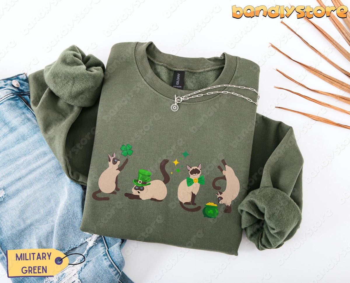 Siamese Cat St Patrick's Day Sweatshirt in military green, folded flat beside jeans, chain and dried leaves.