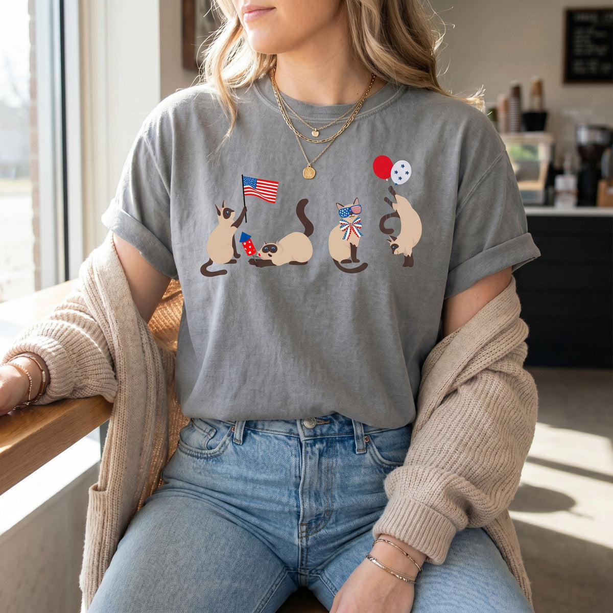 Siamese Cats 4th of July T-Shirt in grey on a seated woman by a cafe window.