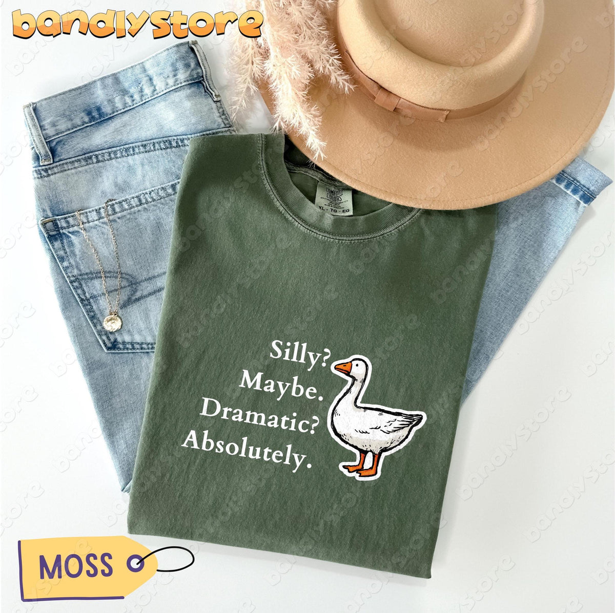 Silly Goose T-Shirt in Moss flat-laid with jeans, beige hat, pampas grass and a gold necklace.