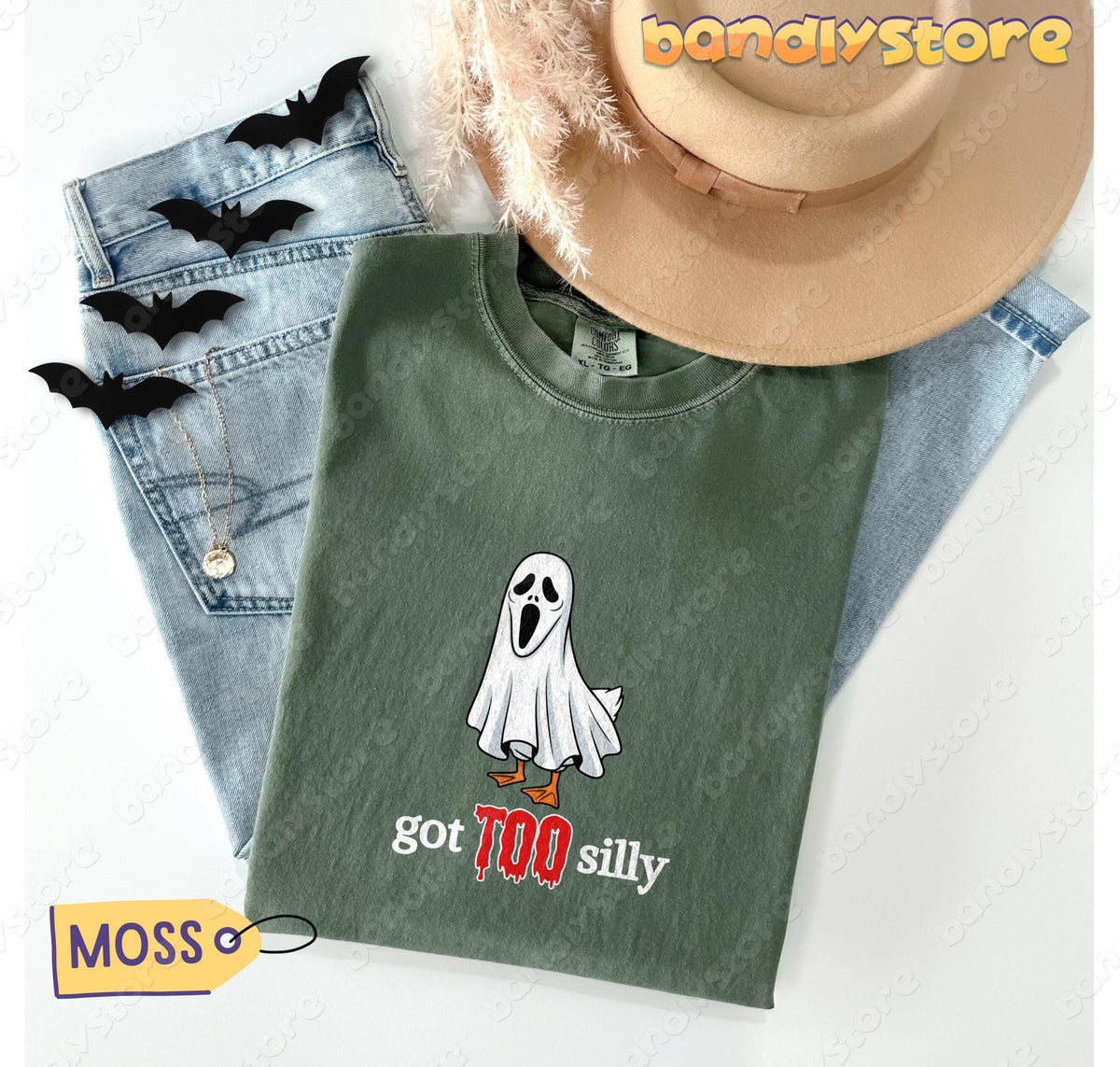 Silly Goose T-Shirt in moss flat-laid with jeans, hat, bat cutouts and pampas grass.