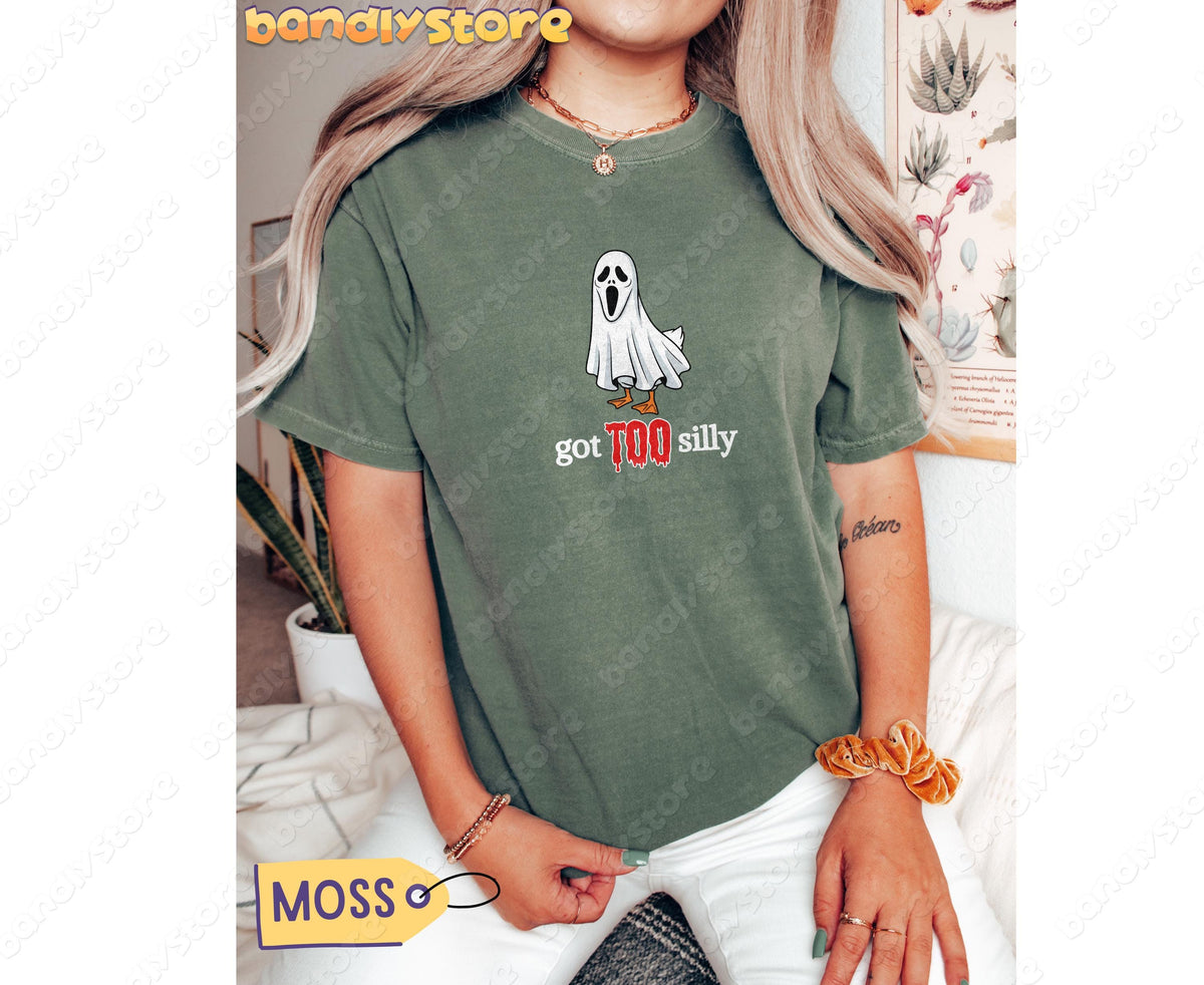 Silly Goose T-Shirt in moss on a seated person facing forward with plants and a poster in the background.