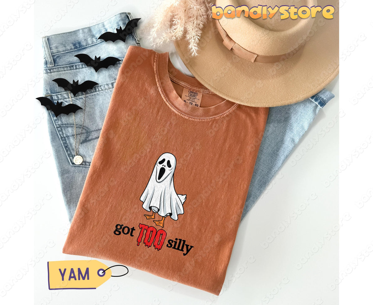 Silly Goose T-Shirt in Yam folded flat beside jeans, a hat, black bats and dried grass.