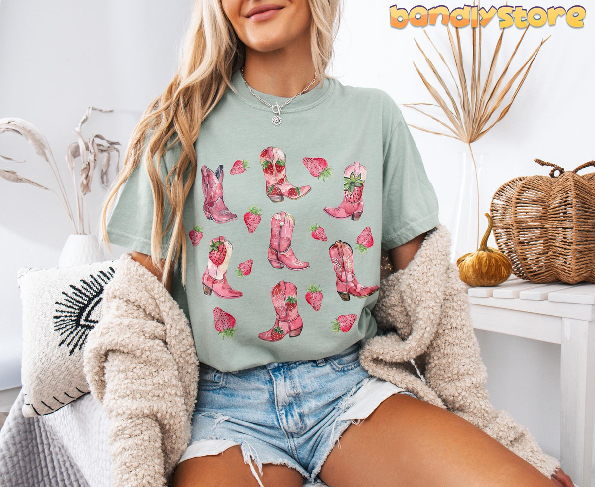 Strawberry Cowgirl Boots T-Shirt in Bay worn by a seated model amid pillows, dried plants and pumpkins.
