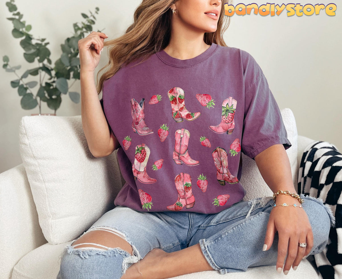 Strawberry Cowgirl Boots T-Shirt in berry on a woman seated on a white sofa beside a plant.